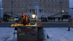 Seorang pedagang kaki lima yang menjual jagung menunggu pelanggan di depan parlemen Yunani di kota Athena (27/12/2021). Pemerintah Yunani diperkirakan akan mengumumkan langkah-langkah baru untuk menahan penyebaran varian Omicron. (AP Photo/Petros Giannakouris)