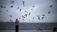 Seorang wanita memberi makan burung camar di kawasan pejalan kaki Galataport di sebelah Bosphorus di Istanbul, Turki (11/1/2022). Tetapi Turki tetap mendesak orang untuk terus memakai masker dan mempraktikkan jarak sosial. (AP Photo/Francisco Seco)