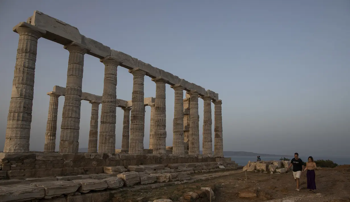 Sepasang pengujung berjalan dekat Kuil Poseidon di Cape Sounion, Athena, Yunani, Senin (18/5/2020). Yunani kembali membuka kota kuno Acropolis serta situs-situs lainnya setelah dua bulan ditutup selama lockdown akibat pandemi virus corona COVID-19. (AP Photo/Petros Giannakouris)