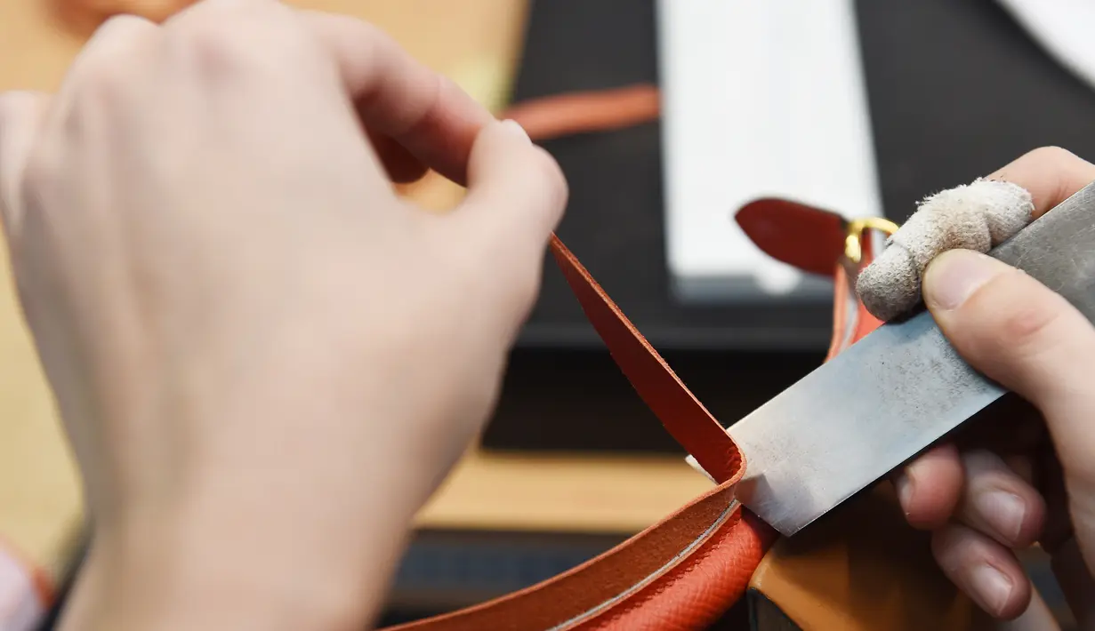 Seorang pengrajin memotong bagian tas saat bekerja di bengkel produsen barang-barang mewah Hermes di Allenjoie, Perancis, Kamis (5/4). Tas Hermes seolah menjadi simbol gaya hidup bagi kaum sosialita di dunia. (SEBASTIEN BOZON/AFP)