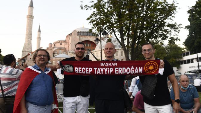 Orang-orang memegang syal dengan nama Presiden Turki Recep Tayyip Erdogan, ketika foto di luar era Bizantium Hagia Sophia, di distrik bersejarah Sultanahmet Istanbul, Kamis, (23/7/2020). Bangunan bersejarah itu resmi dialih fungsi dari museum menjadi masjid pada 10 Juli lalu. (AP Photo/Omer Kuscu)