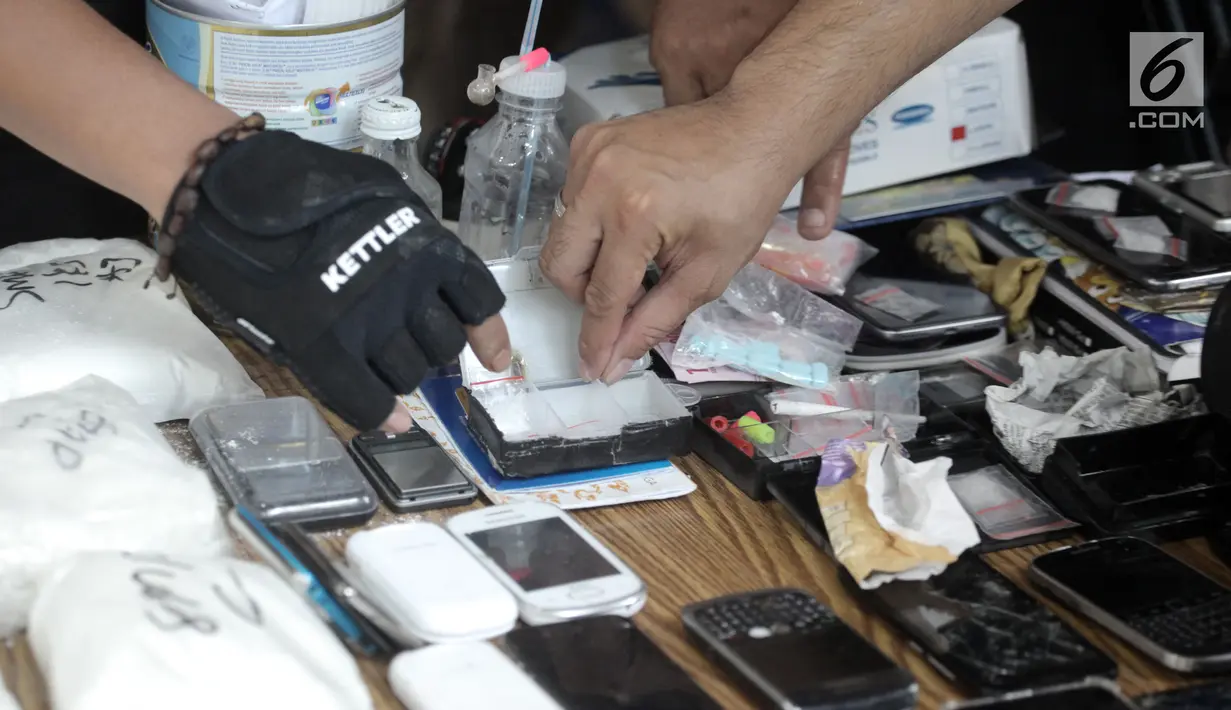 Petugas menunjukkan barang bukti yang berhasil diamankan saat penggerebekan di Kampung Ambon, Cengkareng, Jakarta, Rabu (24/1). Dalam penggerebekan ini ada enam rumah di sejumlah titik yang digeledah. (Liputan6.com/Arya Manggala)