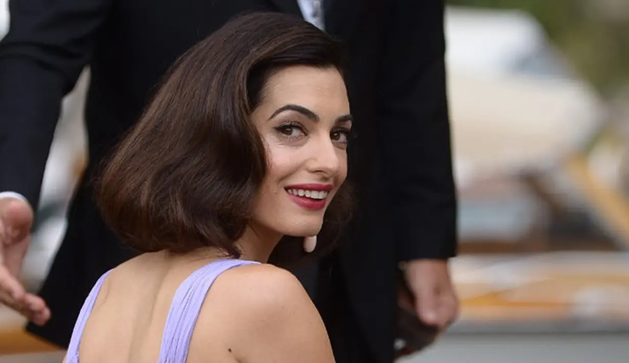 Tampilan keduanya begitu mempesona dengan busana elegan yang dipakai pasangan suami-istri ini. George dengan setelan jasnya dan Amal yang tampak cantik dengan dress berwarna violet rancangan Atelier Versace. (AFP/Filippo Monteforte