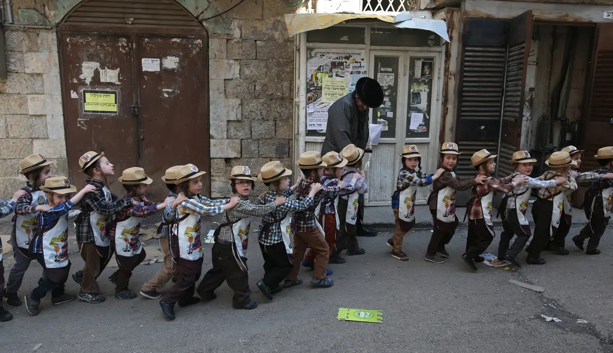 Anak-anak Yahudi ultra-Ortodoks mengenakan kostum berbaris ditepi jalan untuk mengikuti perayaan purim di Yerusalem (8/3). Purim merupakan hari raya atau pesta Yahudi untuk memperingati pembebasan kaum Yahudi dari kekaisaran Persia. (AFP/Menahem Kahana)