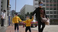 Seorang wanita dan anak-anak yang mengenakan masker dan pelindung wajah berjalan di jalan di Hong Kong, Jumat (4/3/2022). Pemimpin Hong Kong awal pekan ini mengatakan mobilitas orang mungkin dibatasi selama tes covid-19 massal wajib ketika kasus harian mencapai rekor. (AP Photo/Kin Cheung)