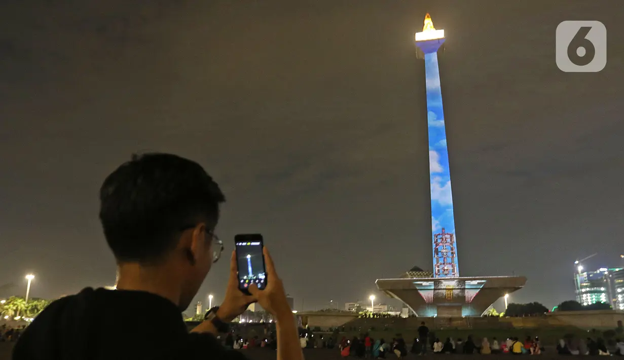 Warga mengambil gambar Tugu Monumen Nasional (Monas)saat berlangsung pertunjukan video mapping di Jakarta, Minggu (22/12/2019). Acara ini berlangsung di pelataran barat Tugu Monas pada 22-31 Desember 2019. (Liputan6.com/Herman Zakharia)