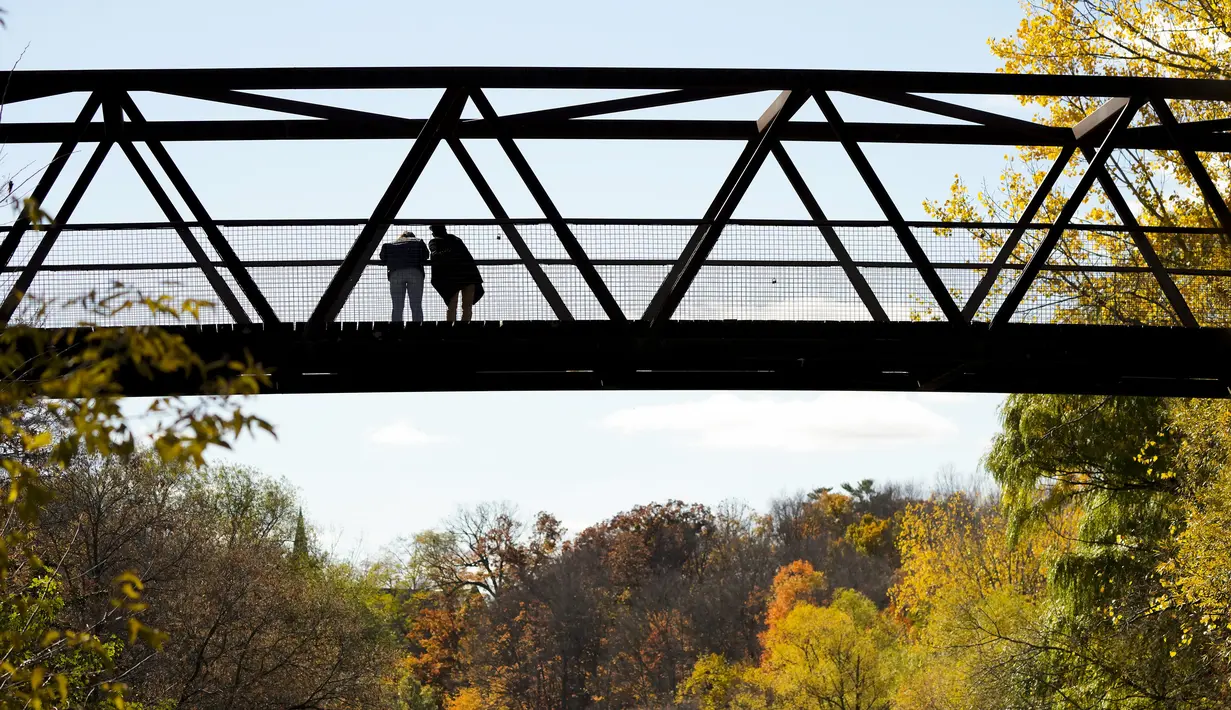 Orang-orang memandangi Sungai Kredit di sebuah jembatan, di antara warna-warni musim gugur di Mississauga, Ontario, pada Kamis, 27 Oktober 2022. (Nathan Denette/The Canadian Press via AP)