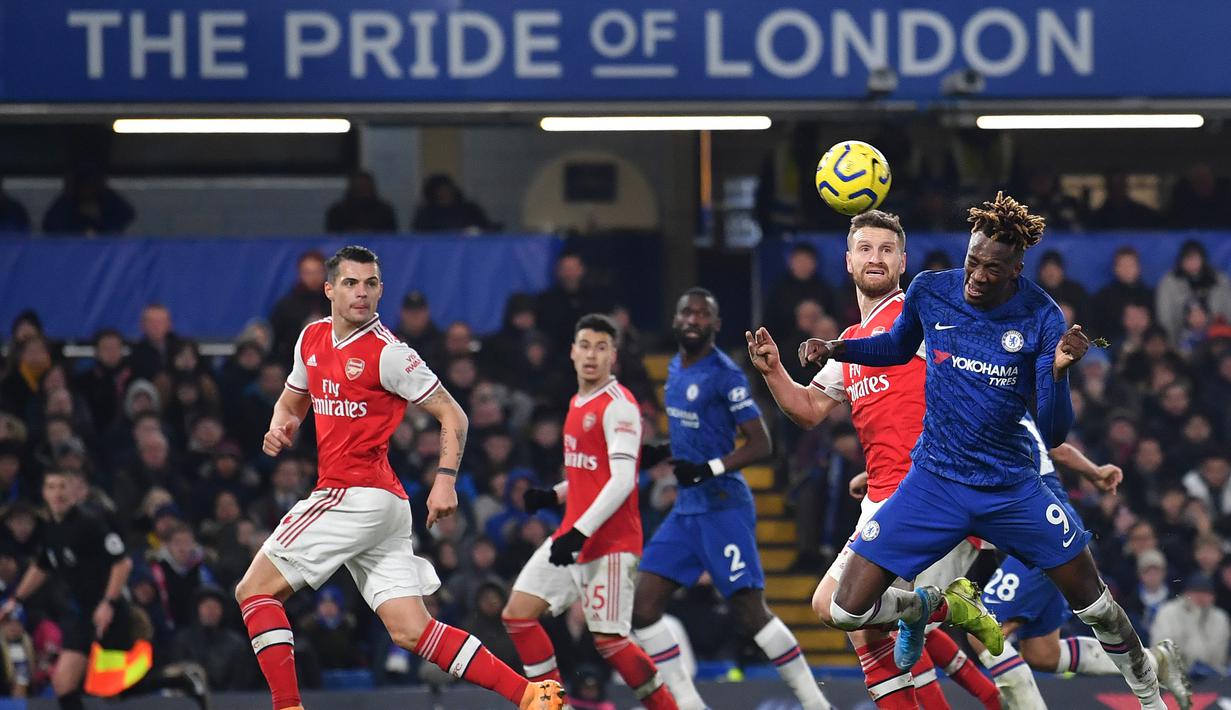 Striker Chelsea, Tammy Abraham, berebut bola dengan bek Arsenal, Shkodran Mustafi, pada laga Premier League pekan ke-24 di Stamford Bridge, London, Rabu (22/1). Arsenal tahan imbang Chelsea 2-2. (AFP/Ben Stansall)
