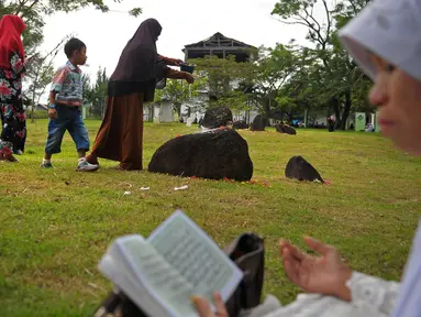 Anggota keluarga menabur bunga di salah satu makam korban tsunami Aceh di sebuah kuburan massal di Aceh, Senin (26/12). Warga Aceh memperingati 12 tahun gempa dahsyat berkekuatan 9,3 SR disusul tsunami pada Minggu 26 Desember 2004 (CHAIDEER MAHYUDDIN/AFP)