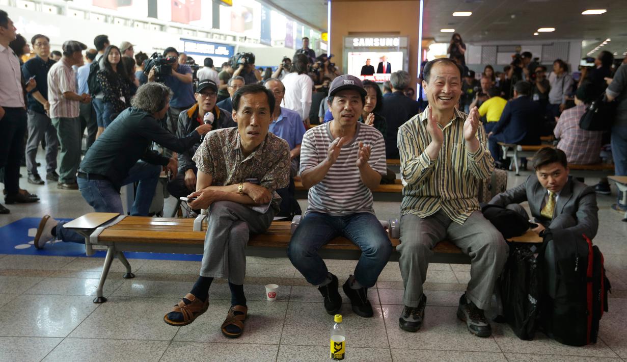 Orang-orang bertepuk tangan melihat berita pertemuan Presiden AS Donald Trump dan pemimpin Korea Utara Kim Jong-un di Seoul Railway Station, Korea Selatan, Selasa (12/6). Untuk pertama kalinya dalam sejarah, Trump dan Kim bertemu. (AP/Ahn Young-joon)