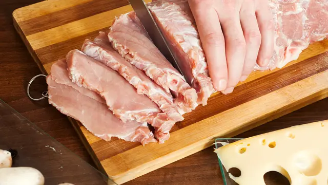 Sebuah tangan sedang memotong daging sapi mentah (Foto Dok: Freepik/bearfotos)