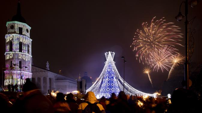 Kembang api menerangi langit di atas pohon Natal yang menyala di Lapangan Katedral di Vilnius, Lithuania selama perayaan Tahun Baru, Rabu (1/1/2020). (AP Photo/Mindaugas Kulbis)