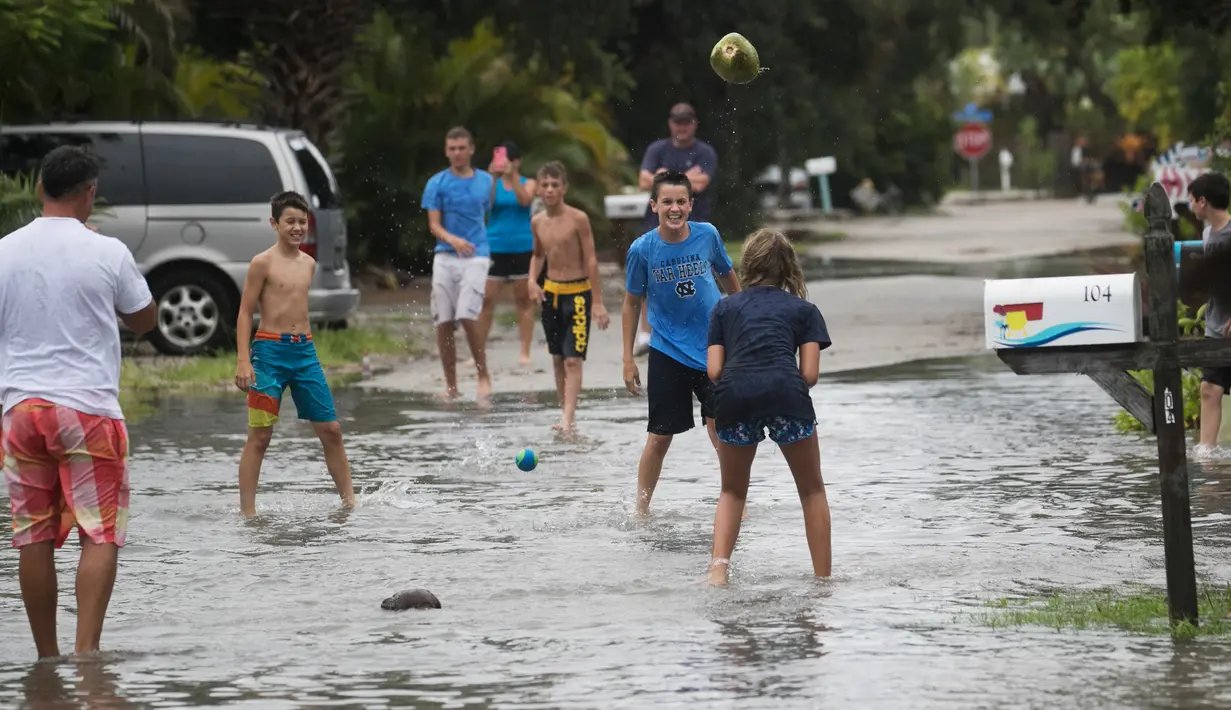 Suasana keluarga Wilkins saat bermain dalam genangan banjir di jalan Pantai Fort Myers, Florida, Senin (31/7). Gubernur Rick Scott mengumumkan keadaan darurat untuk 31 negara bagian Florida selatan dan tengah. (The News-Press via AP/Andrew West)