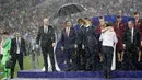 Presiden Rusia, Vladimir Putin dilindungi oleh seorang pemandu yang memegang payung sementara para pejabat lainnya basah kuyup saat hujan turun selama penyerahan medali dan trofi Piala Dunia 2018 di Stadion Luzhniki, Minggu (15/7). (AP/Matthias Schrader)