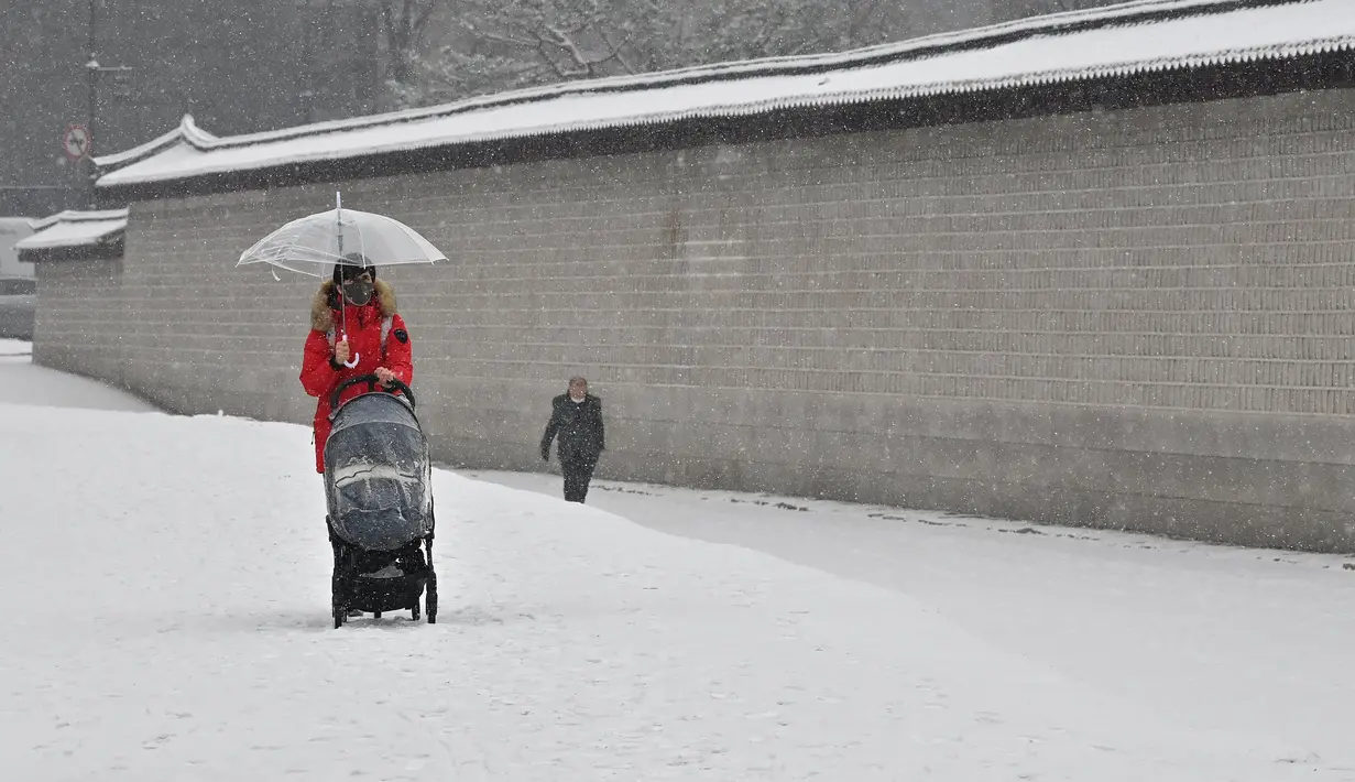 Seorang wanita mengendarai kursi dorong di sepanjang jalan yang tertutup salju di pusat kota Seoul (19/1/2022). Peringatan salju tebal telah dikeluarkan di seluruh kota pada pukul 9 pagi. (AFP/Jung Yeon-je)