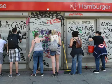 Sejumlah warga membersihkan jendela bank dari coretan aksi protes KTT G20 di Hamburg, Jerman, Minggu (9/7). Demonstrasi yang mewarnai gelaran KTT G20 di Hamburg sejak Kamis waktu setempat itu menyebabkan sejumlah kerusakan. (Christof Stache/AFP)