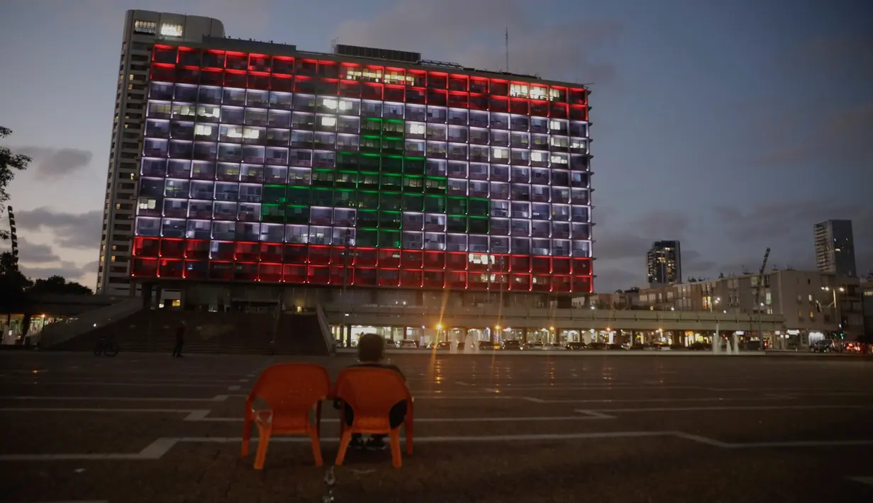 Seorang perempuan Israel duduk saat Gedung Balai diterangi dengan bendera Lebanon di Tel Aviv, Rabu (5/8/2020). Cahaya bendera Lebanon diproyeksikan sebagai bentuk solidaritas atas ledakan dahsyat di Beirut yang menghebohkan dunia. (AP Photo/Sebastian Scheiner)
