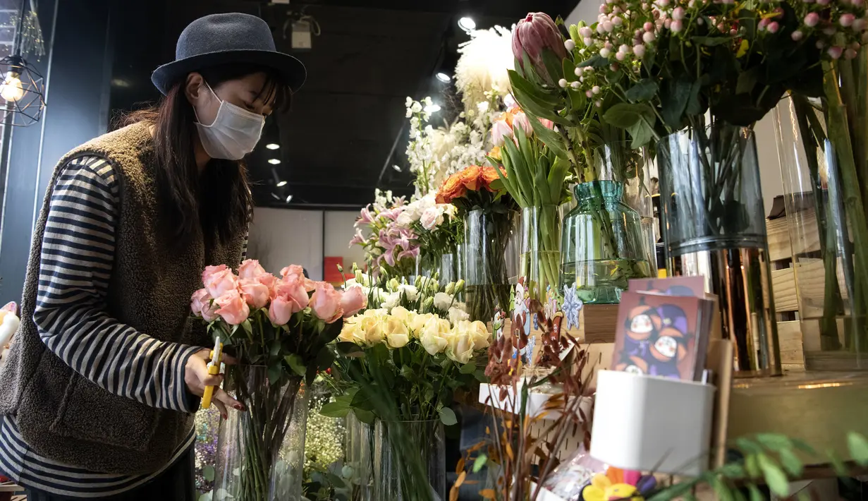 Penjual bunga Zhao Yuanyuan mengenakan masker mengatur bunga menjelang Hari Valentine di tokonya di Shanghai (12/2/2020). Pasangan-pasangan yang merayakan Hari Valentine di seluruh China dibayangi wabah virus corona COVID-19. (AFP Photo/Noel Celis)