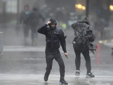 Pejalan kaki diterpa angin dan hujan saat menyeberang jalan di Boston, Amerika Serikat, Senin (18/12/2023). Badai yang bergerak di Pantai Timur membawa hujan lebat dan angin kencang ke Timur Laut pada hari Senin, mengancam banjir dan memadamkan listrik ke ratusan ribu rumah. (AP Photo/Steven Senne)