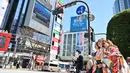 Seorang wanita berpakaian kimono (kanan) mengambil foto saat dirinya dan yang lain menunggu untuk menyeberangi persimpangan pejalan kaki yang terkenal di distrik Shibuya, Tokyo pada 20 Maret 2019. (Photo by CHARLY TRIBALLEAU / AFP)