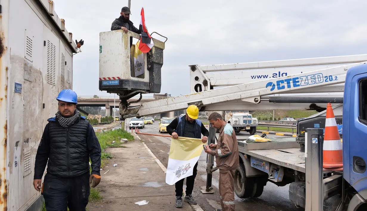 Pekerja mengibarkan bendera Irak dan Takhta Suci Vatikan di tiang-tiang jalan di kota Mosul, Irak, Kamis (4/3/2021). Pemimpin Tertinggi Umat Katolik Paus Fransiskus memulai kunjungan bersejarah ke Irak pada Jumat (5/3), meskipun menghadapi pandemi Covid-19 dan ancaman keamanan. (Zaid AL-OBEIDI/AFP)