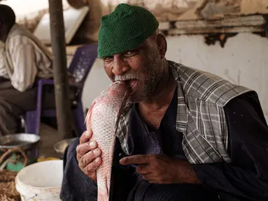 Pedagang ikan bercanda menggigit seekor ikan ketika ia difoto di sebuah pasar ikan di dekat Sungai Nil, di kota kembar Khartoum, Omdurman (24/6/2019). Omdurman merupakan kota terbesar di Sudan memiliki jumlah penduduk sebanyak 1,2 juta jiwa (1993). (AFP Photo/Yasuyoshi Chiba)