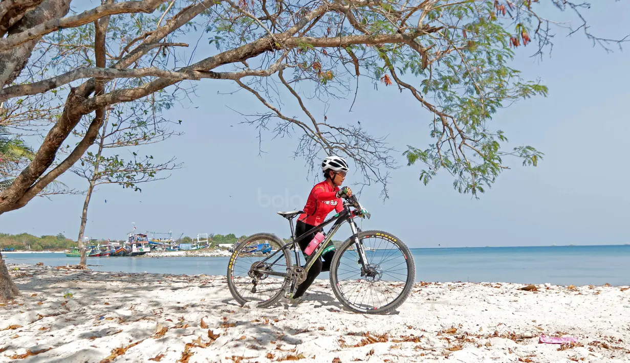Seorang pebalap wanita Mountain Bike Cross Country Marathon mendorong sepedanya saat melintasi pasir pada Festival Pesona Tanjung Lesung 2017 di Tanjung Lesung, Banten (23/9/2017). MTB XCM tersebut menempuh jarak 48 km. (Bola.com/Nicklas Hanoatubun)