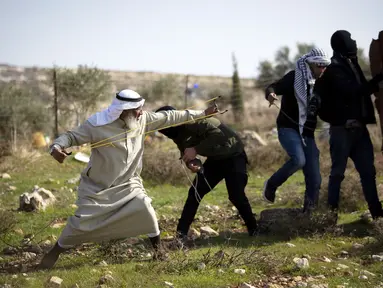 Pengunjuk rasa Palestina menggunakan ketapel untuk melemparkan batu ke arah pasukan Israel selama protes terhadap permukiman Israel, di desa Deir Jarir Tepi Barat, utara Ramallah, Jumat (1/1/2021). Setidaknya 16 warga Palestina terluka akibat bentrokan tersebut. (AP Photo/Majdi Mohammed)