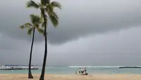 Para pengunjung pantai terlihat dengan latar belakang awan badai, di Pantai Waikiki, Honolulu (6/12/2021). Badai kuat yang membawa angin kencang dan hujan yang sangat deras membanjiri jalan-jalan dan meruntuhkan kabel listrik dan cabang-cabang pohon di seluruh Hawaii. (AP Photo/Marco Garcia)