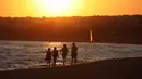 Sejumlah orang berjalan saat matahari terbenam di pantai Sampieri, Sisilia, (31/7). (AFP Photo/Ludovic Marin)