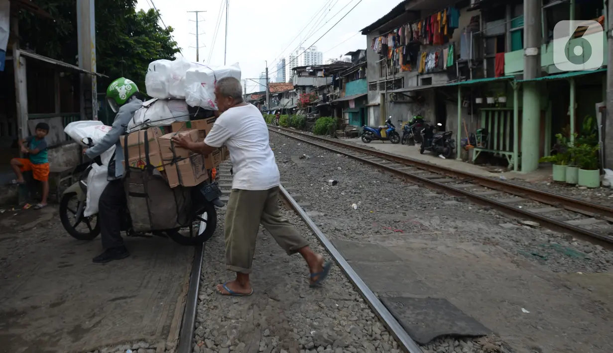 Penjaga perlintasan kereta api tanpa palang pintu, Wandi, membantu pengendara menyeberangi perlintasan di Kawasan Petamburan, Jakarta, Jumat (4/6/2021). Sudah 10 tahun, Bapak Wandi menjaga palang pintu perlintasan kereta api di kawasan tersebut. (merdeka.com/Imam Buhori)
