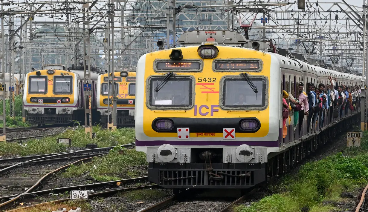 Penumpang berdiri pada pintu gerbong kereta yang terbuka saat mereka melakukan perjalanan dengan kereta lokal di Mumbai, India, Kamis (8/9/2022). (Indranil MUKHERJEE/AFP)