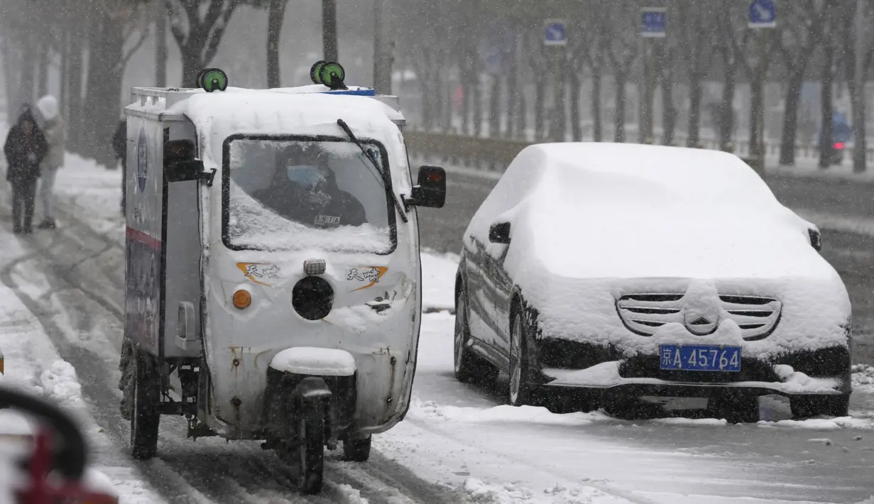 Seorang pengantar melewati sebuah mobil yang diselimuti salju di Beijing, Minggu (7/11/2021). Badai salju awal musim telah menyelimuti sebagian besar China utara termasuk ibu kota Beijing, mendorong penutupan jalan dan pembatalan penerbangan. (AP Photo/Ng Han Guan)