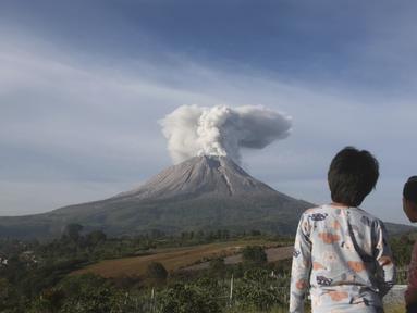 Dua orang Anak menyaksikan Gunung Sinabung memuntahkan material vulkanik saat meletus di Karo, Sumatera Utara, Kamis (11/3/2021). Gunung berapi tersebut mengeluarkan longsoran awan gas membakar yang mengalir menuruni lerengnya saat terjadi letusan pada hari Kamis. (AP Photo/Binsar Bakkara)