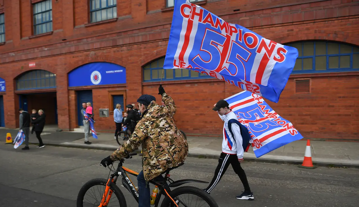 Para fans Glasgow Rangers dengan bersepeda dan berjalan kaki mengibarkan bendera klub di luar Ibrox Stadium (7/3/2021) untuk merayakan keberhasilan tim kesayangan mereka merebut gelar Liga Utama Skotlandia setelah memimpin 20 poin dari saingan terdekat, Glasgow Celtic. (AFP/Andy Buchanan)