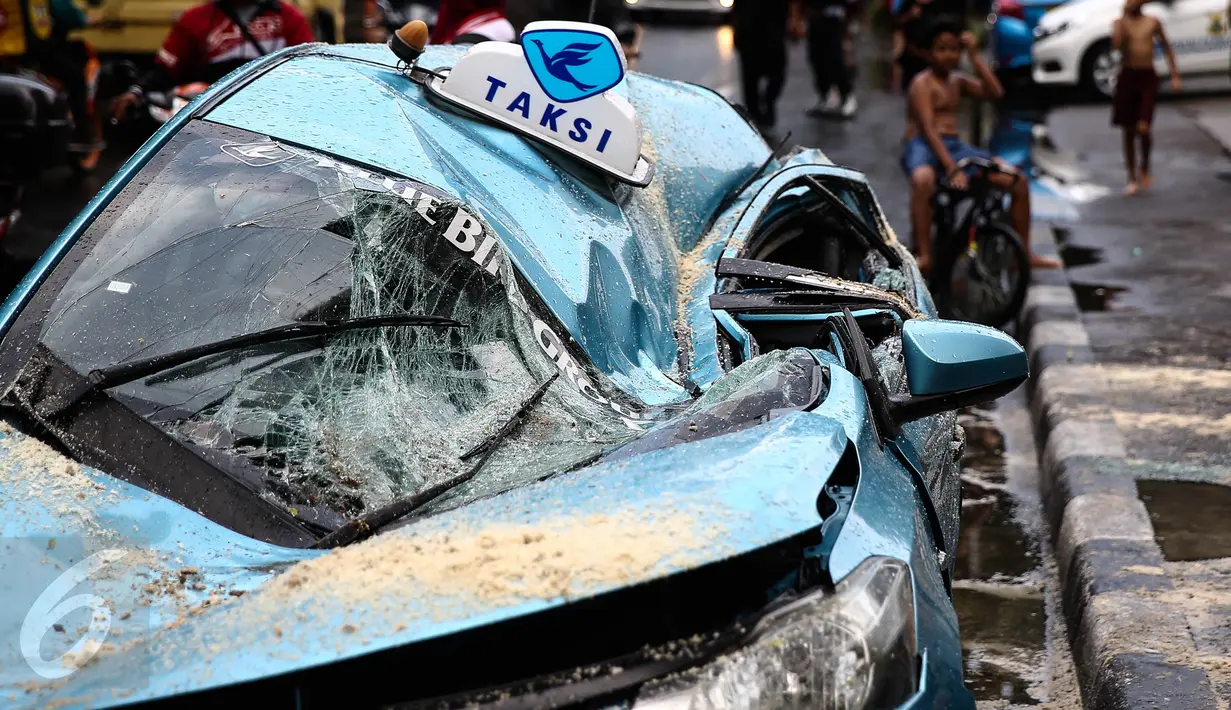 Kondisi taksi yang ringsek tertimpa pohon tumbang akibat hujan deras disertai angin kencang di Jalan Taman Kebon Sirih, Jakarta, Selasa (30/8). Batang pohon itu menimpa kap mesin dan kursi penumpang di samping kemudi. (Liputan6.com/Faizal Fanani)