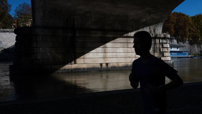 Seorang pria berlari di sepanjang sungai Tiber ketika pemerintah memberlakukan langkah-langkah yang lebih ketat untuk mengekang penyebaran Covid-19 (novel coronavirus), di Roma tengah (17/11/2020). (AFP/Tiziana Fabi)