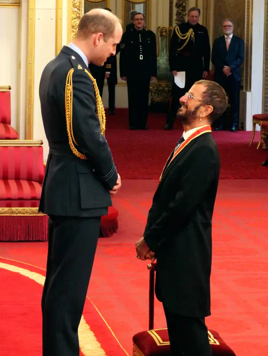 Ringo Starr berbincang dengan Pangeran William setelah menerima gelar kebangsawanan di Istana Buckingham, di London, Inggris (20/3). Ringgo diberi gelar 'Sir' atas jasanya dalam dunia musik. (Yui Mok / PA via AP)