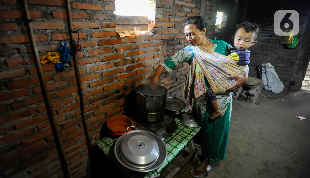 Warga menggendong bayi saat memasak menggunakan energi yang berasal dari biogas di Desa Dompyong, Trenggalek, Jawa Timur, Minggu (3/9/2023). (merdeka.com/Arie Basuki)