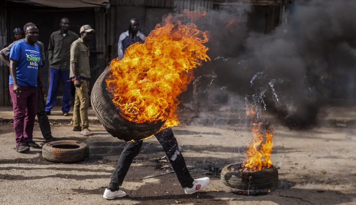 Seorang pengunjuk rasa membawa ban yang terbakar untuk memblokir jalan di lingkungan Kibera di Nairobi, Kenya Rabu, 12 Juli 2023. Pengunjuk rasa anti-pemerintah berdemonstrasi di sejumlah kota Kenya menentang pajak yang baru diberlakukan dan biaya hidup. (AP Photo/Samson Otieno)
