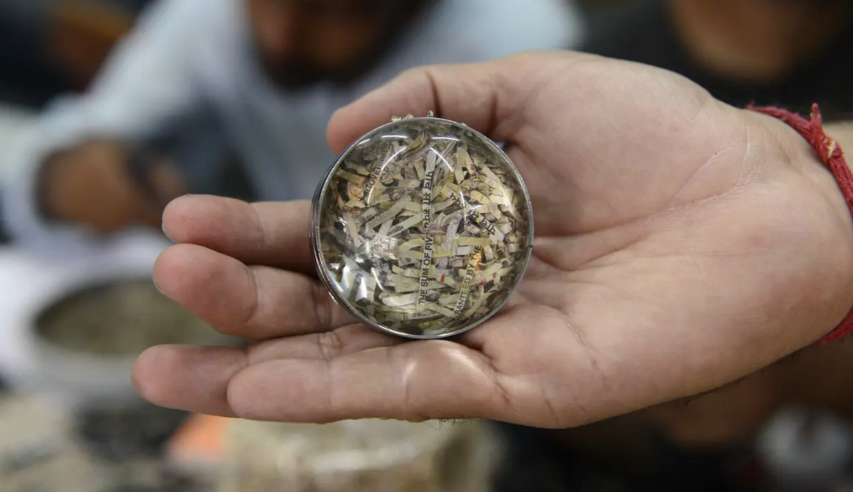 Seorang pria menunjukkan potongan uang kertas yang telah dibentuk, Ahmedabad, India (26/4). Ide kreatif ini berawal dari pemanfaatan mata uang kertas 500 dan 1.000 Rupee yang ditarik pemerintah India pada 2016 silam. (AFP PHOTO/SAM PANTHAKY)