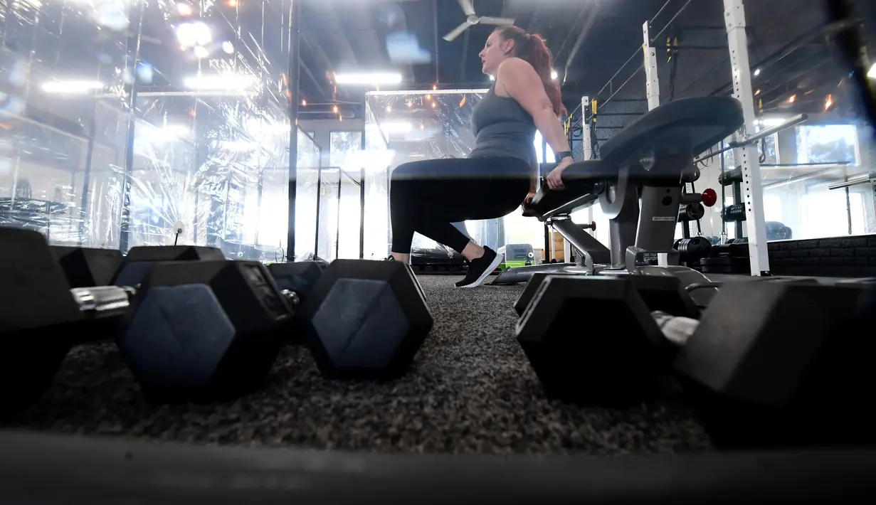 Seorang perempuan berolahraga dalam kotak plastik yang disediakan oleh Inspire South Bay Fitness di Redondo Beach, California pada 15 Juni 2020. Ruangan gym dengan plastik sebagai pemisah itu agar pengunjung dapat tetap berolahraga sambil tetap menjaga jarak fisik. (FREDERIC J. BROWN / AFP)