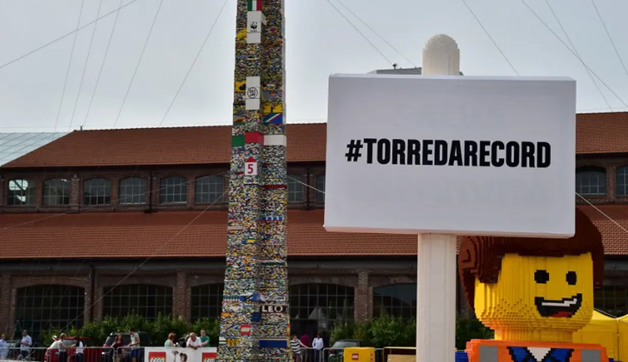 Karakter Lego berpose  di depan sebuah menara lego setinggi 35.50 meter, Itali, Minggu (21/6/2015).  Menara ini dibangun oleh ribuan relawan menggunakan sekitar 580.000 lego dan mendapat sertifikat rekor dunia dari Guinness. (AFP Photo/Giuseppe Cacace) 
