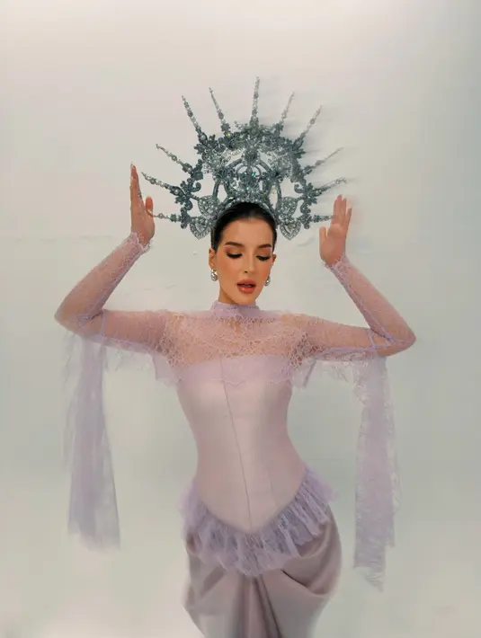 Dengan kedua tangan terangkat dan mata menunduk, Tasya memamerkan potongan lengan renda yang menjuntai panjang. Gaun lilac dengan korset satin yang membentuk siluet, rok bergaya draping, dan crown silver bertabur mutiara menegaskan kesan anggun sekaligus kuat. [@tasyafarasya]