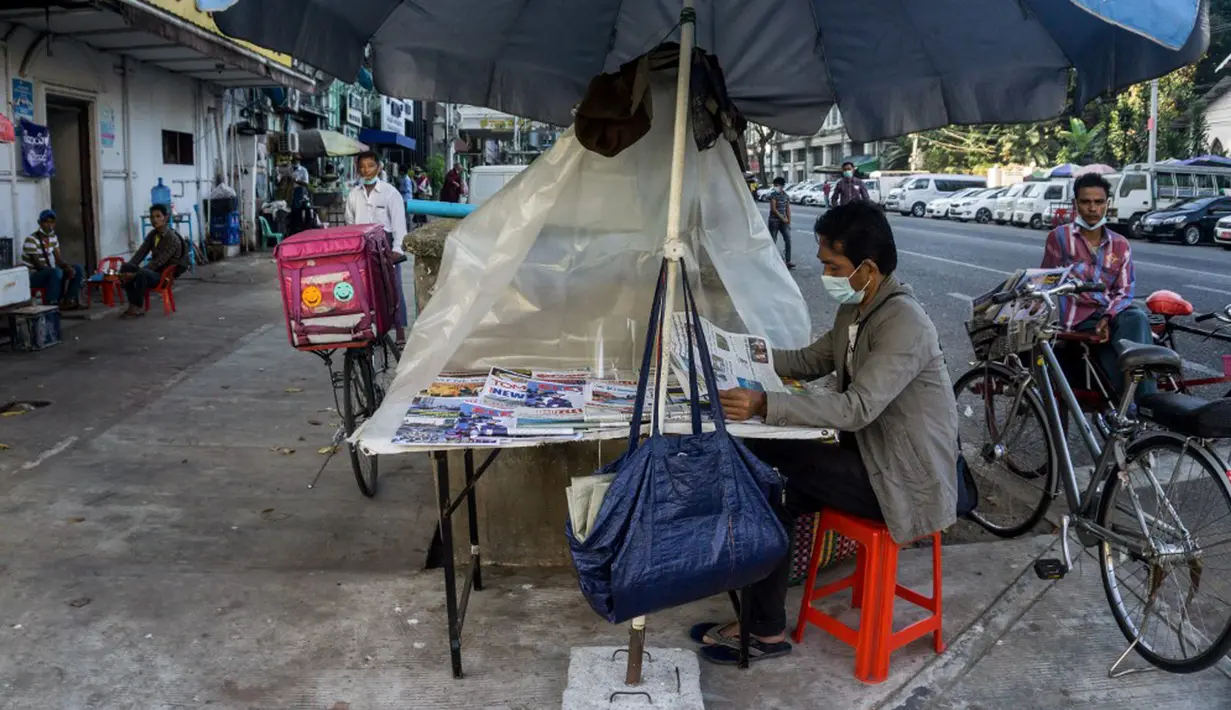 Seorang pria membaca koran di kiosnya sehari setelah militer Myanmar merebut kekuasaan, Yangon, Myanmar, Selasa (2/2/2021). Militer Myanmar menahan pemimpin yang terpilih secara demokratis Aung San Suu Kyi dan memberlakukan keadaan darurat satu tahun. (STR/AFP)