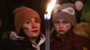 Seorang wanita dan seorang anak memegang obor saat demonstrasi untuk Ukraina yang diselenggarakan oleh Greenpeace di Heroes Square, Budapest, Hungaria, 9 Maret 2022. Lebih dari 1,5 juta orang telah menyeberang dari Ukraina ke negara-negara tetangga. (AP Photo/Anna Szilagyi)