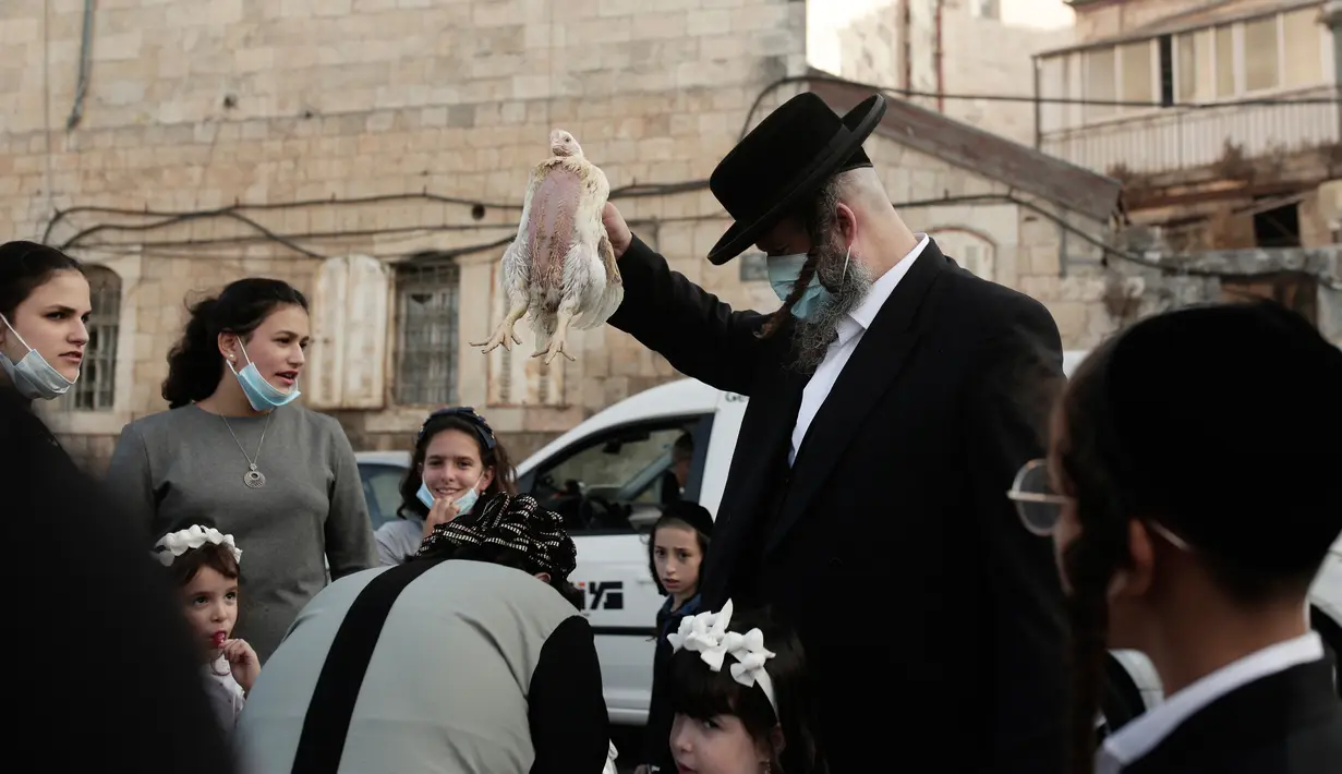 Seorang pria Yahudi ultra-Ortodoks mengayunkan ayam di atas kepala keluarganya sebagai bagian dari ritual Kaparot di Yerusalem, Rabu (23/9/2020). Tradisi itu digelar sebelum perayaan Yom Kippur atau hari Penebusan dosa, hari paling suci dalam tahun Yahudi. (AP Photo/Maya Alleruzzo)