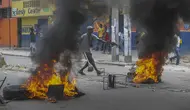 Seorang pria menambahkan puing-puing untuk dibakar di barikade ban yang terbakar yang dipasang oleh pengunjuk rasa selama demonstrasi menuntut Perdana Menteri Haiti Ariel Henry mundur dan menyerukan kualitas hidup yang lebih baik, di Port-au-Prince, Haiti, Senin (29/8/2022). (AP Photo/Odelyn Joseph)