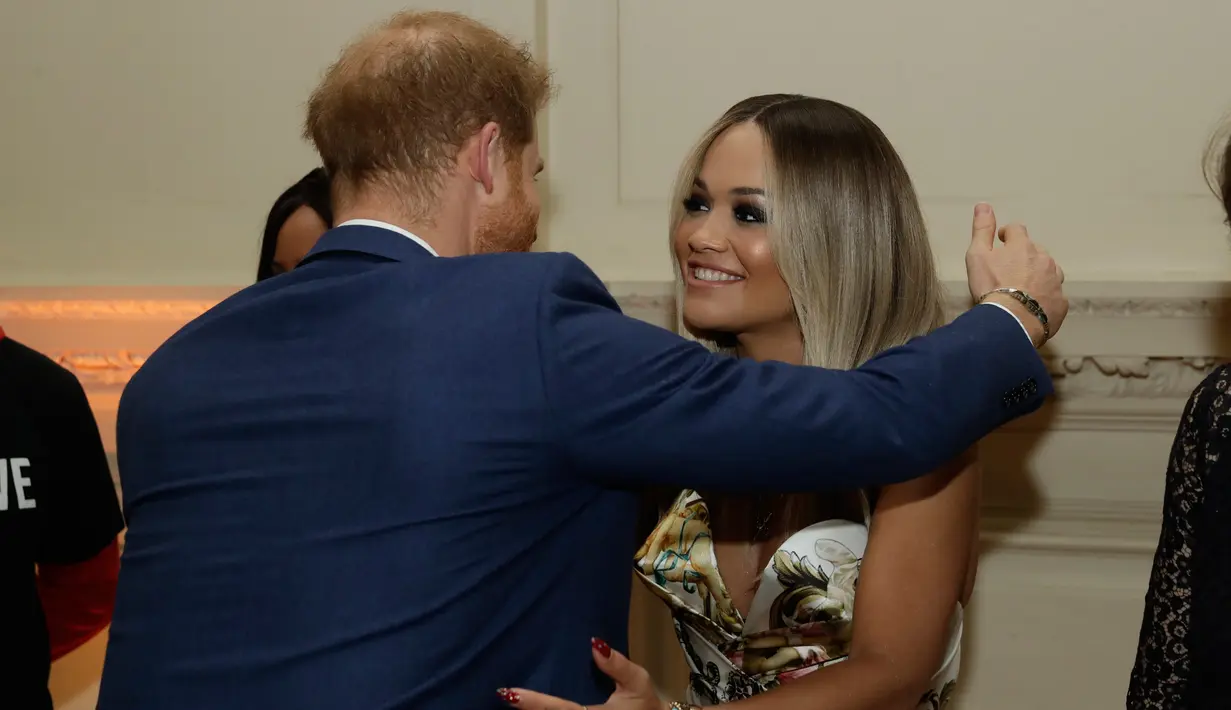 Pangeran Harry memeluk penyanyi Rita Ora sebelum konser yang diadakan badan amal Sentebale di Hampton Court Palace, London (11/6/2019). Rita Ora tampil seksi mengenakan gaun mini glamor dengan pola kerubin dengan sandal bertali. (AP Photo/Matt Dunham)