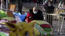 Seorang pria yang mengenakan masker menggendong seorang anak menonton keluarga naik kereta mainan di sebuah taman hiburan di Beijing (17/1/2022). Jumlah bayi yang lahir di China terus menyusut tahun lalu, seiring menyusutnya jumlah tenaga kerja. (AP Photo/Andy Wong)